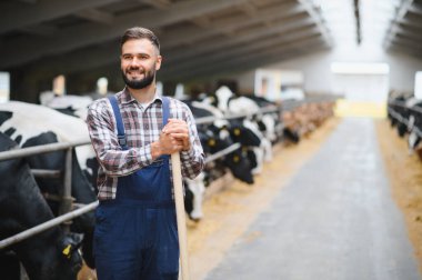 Bir yaba tutan bir çiftçinin portresi, arka planda sığırlarla bir inek ahırında gülümsüyor, tarımı ve çiftlik hayvanlarını temsil ediyor.