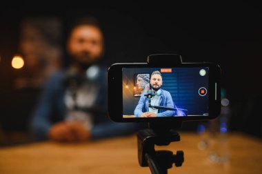 Video blogcusu modern bir stüdyoda içerik yakalıyor, yüksek kaliteli ses ve görüntü için akıllı telefon ve mikrofon kullanıyor