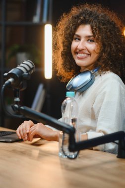 Genç bir kadın, yüksek kaliteli ses için profesyonel mikrofon ve kulaklık kullanarak çevrimiçi kanalı için video içeriği oluşturuyor.