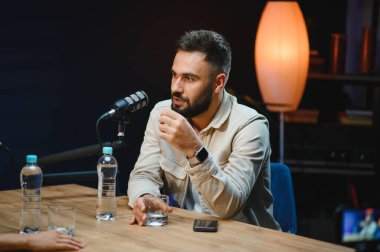 Profesyonel bir stüdyoda podcast kaydederken mikrofona konuşan içerik yaratıcısı, izleyicileriyle iletişim kuruyor ve değerli sezgilerini paylaşıyor.