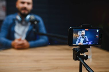 Video blogcusu, iyi donanımlı bir stüdyo ortamında tripoda monte edilmiş akıllı bir telefonla içeriği yakalıyor.