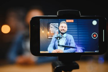 Video blogcusu akıllı telefon ve mikrofonla içerik oluşturmaya çalışıyor, modern ev stüdyosunda dinamik videolar kaydediyor.
