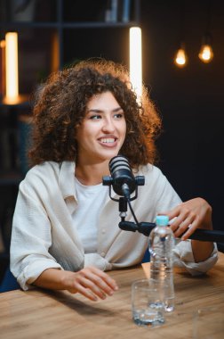 İçerik yaratıcısı ses içeriğini ev stüdyosunda kaydediyor, profesyonel mikrofon ve ekipman kullanıyor, konuşuyor ve gülümsüyor