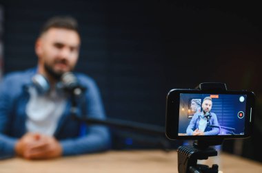 Profesyonel bir stüdyoda içerik yakalayan video blogcusu, yüksek kaliteli ses ve video için akıllı telefon ve mikrofon kullanıyor