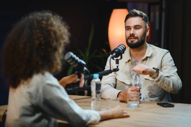 İki içerikli yaratıcı, bir erkek ve bir kadın, profesyonel bir stüdyoda bir podcast kaydediyor, sohbet ediyorlar ve uzmanlıklarını paylaşıyorlar.