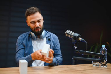 Erkek podcaster profesyonel bir stüdyoda canlı yayında yeni bir ürün sunuyor, çevrimiçi bir izleyici kitlesine hitap ediyor.
