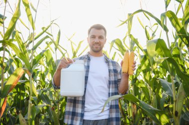 Mısır tarlasında mısır koçanı ve böcek ilacı şişesini gösteren çiftçi, ekinlerin korunmasını ve yüksek verim sağlıyor.