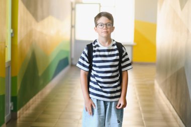 Okul koridorunda yürüyen ve bilgiye ve öğrenmeye hazır genç bir öğrencinin portresi.