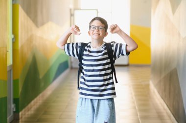 Gülümseyen öğrenci okul koridorunda kaslarını esnetiyor, okul ruhunun özgüven ve gururunu somutlaştırıyor.