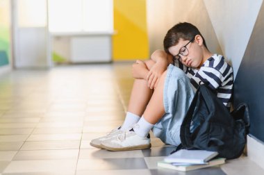 Bir okul koridorunda kabadayılığın acısını yaşayan, kendini yalnız hisseden, korku ve üzüntü içinde ağlayan bir öğrenci.