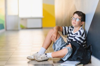 Öğrenci çocuk yerde tek başına oturuyor, sınıf arkadaşlarının zorbalığından acı çektikten sonra ağlıyor, üzüntü ve yalnızlık hissediyor.