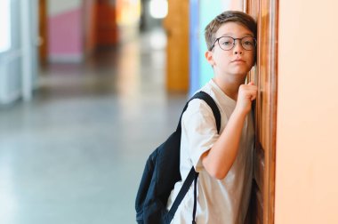 Okul çantalı çocuk teneffüste okul koridorunda duruyor. Yüzünde düşünceli bir ifade var.