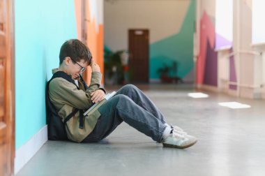 Okul koridorunda yerde oturan, elinde kitaplarla zorbalık gördükten sonra ağlayan bir çocuk.