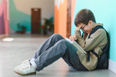 Öğrenci çocuk yerde oturuyor, ağlıyor ve okulda zorbalığın ağırlığını hissediyor, yalnızlığın ve korkunun acısını somutlaştırıyor.