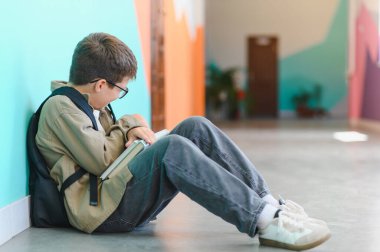 Okul koridorunda yerde oturan ve sınıf arkadaşlarının zorbalığına uğradıktan sonra ağlayan üzgün öğrenci.