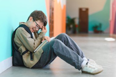 Okullu çocuk okul koridorunda yerde otururken gülüyor ve elleriyle yüzünü saklıyordu.