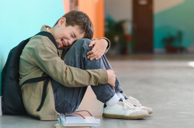 Sınıf arkadaşlarının zorbalığından ve çocuk istismarından acı çektikten sonra okulda yerde ağlayan üzgün öğrenci.