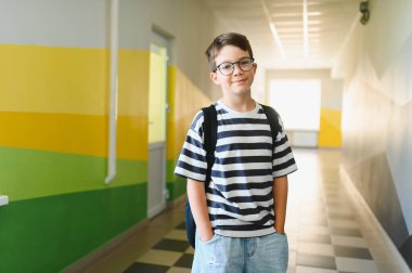 Sırt çantalı bir çocuğun portresi. Okul koridorunda duruyor. Öğrenmeye ve eğitime hazır.