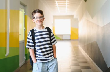 Okulunun koridorunda duran neşeli bir öğrencinin portresi, yeni bir öğrenme gününe hazır.