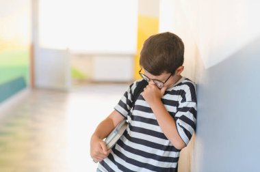 Okul koridorunda elinde kitap tutan ve ağlayan üzgün öğrenci, sınıf arkadaşlarının zorbalığının ve tacizinin ağırlığını hissediyor.