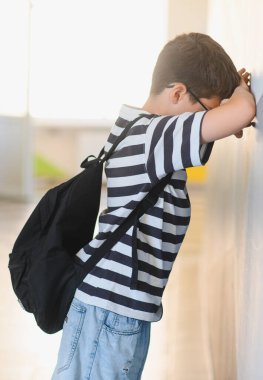 Ağlayan okul çocuğu duvara yaslanıyor, zorbalığın ağırlığını hissediyor, izolasyon ve eğitimin duygusal sıkıntılarını somutlaştırıyor.