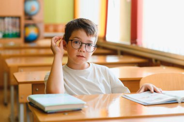 İlkokul öğrencisi gözlük takıyor. Ders sırasında dikkatlice dinliyor, kulağına kalem dayıyor.