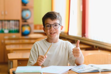 Sınıfta masa başında oturan, elinde kalem tutan, ders kitabı okuyan, öğrenme sürecinden zevk alan zeki bir öğrenci.