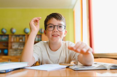 Gözlüklü akıllı çocuk elini kaldırıyor ve ilkokul dersine aktif olarak katılıyor.
