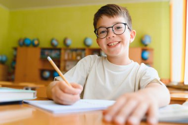 Not defterine yazan mutlu ilkokul öğrencisi, gülümsüyor ve okulda eğleniyor.