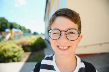 Gözlüklü ve sırt çantalı neşeli bir öğrencinin portresi okula dönüşünün keyfini çıkarıyor.