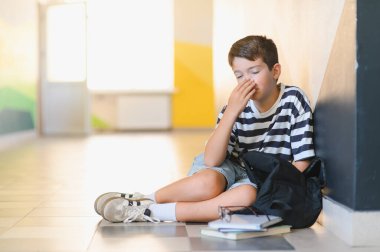 Okulda zorbalığa uğradıktan sonra sırt çantası ve kitaplarıyla yerde oturup ağlayan ve yüzünü kapatan bir öğrenci.