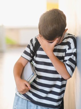 Okul koridorunda sınıf arkadaşlarının zorbalığı yüzünden ağlayan ve kitap tutan çocuk.