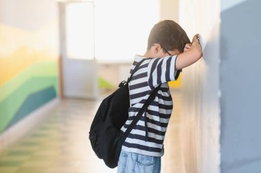 Okulun koridorunda ağlayan üzgün çocuk, sınıf arkadaşlarının zorbalığının ağırlığını hissediyor, izolasyon ve duygusal acı yaşıyor.