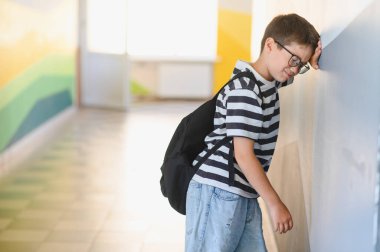 Okul koridorunda duvara yaslanmış, zorbalıktan ağlayan ve sınıf arkadaşlarının tacizinden bunalmış hisseden bir öğrenci.