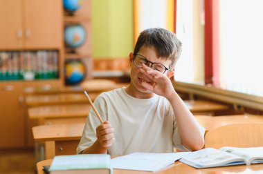 Yorgun bir öğrenci ders sırasında gözlerini ovuşturuyor, elinde kalem tutarken yorgunluk ve konsantrasyonla mücadele ediyor.