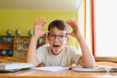 Öğrenci sınıfında masasında ders çalışırken komik bir surat ifadesi takınıyor, okula geri dönmenin tadını çıkarıyor.