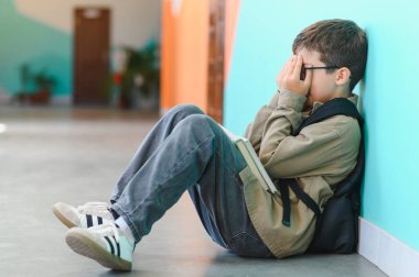 Genç okul çocuğu ağlıyor ve elleriyle yüzünü örtüyor. Okuldaki sınıf arkadaşlarının zorbalığına maruz kalıyor.