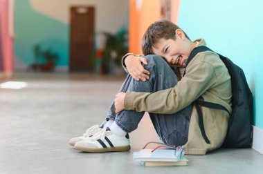 Üzgün liseli çocuk ağlıyor ve dizlerine sarılıyor, okulda zorbalığın ağırlığını hissediyor, korku ve yalnızlık duygularıyla boğuşuyor.