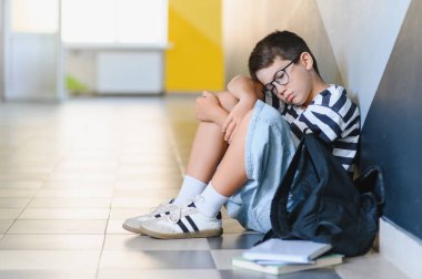 Okul koridorunda tek başına oturan üzgün öğrenci sınıf arkadaşları tarafından hırpalandıktan sonra ağlıyor duygusal sıkıntı ve yalnızlık yaşıyor.