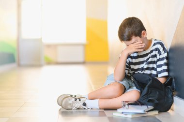 Okulun koridorunda yerde oturup ağlayan üzgün çocuk, yüzünü eliyle, sırt çantasıyla ve kitaplarıyla örterek sınıf arkadaşlarının zorbalığının kurbanı oldu.