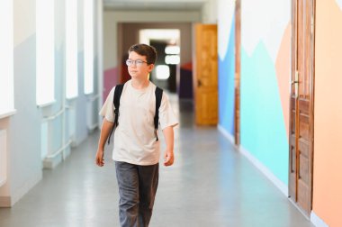 Okul çocuğu okul koridorunda sırt çantasıyla yürüyor, tatilin tadını çıkarıyor ve çocukluğun kaygısız ruhunu kucaklıyor.