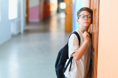 Okul koridorunda sırt çantalı bir ilkokul öğrencisi, düşünceli ve düşünceli görünüyor.