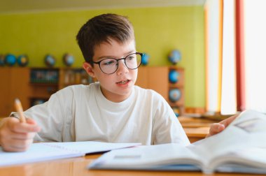 Genç bir öğrenci kitap okuyor ve sınıfta notlar alıyor. Derinlemesine okul ödevlerine odaklanmış ve bilgiyi coşkuyla özümsüyor.