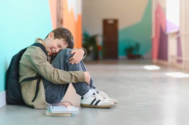 Sınıf arkadaşlarının zorbalığından, çocuk istismarından ve zorbalığından acı çektikten sonra okulda yerde tek başına ağlayan üzgün okul çocuğu.