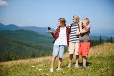 Bir grup çocuk yaz tatilinde dağlarda yürüyüş yapıyor, kamera ve dürbün kullanıyor, doğayı keşfediyor ve birlikte eğleniyorlar.
