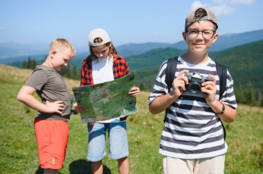 Bir grup çocuk yaz tatilini dağlarda gezintiye çıkarak, harita kullanarak ve klasik kamerayla fotoğraf çekerek geçiriyorlar.