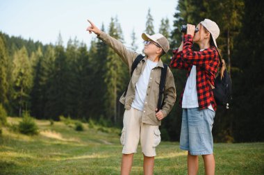 İki genç yürüyüşçü, bir erkek ve bir kız, bir ormanı araştırıyorlar, dürbünle ve açık hava maceraları sırasında uzak manzaraları gösteriyorlar.