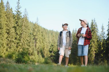 Sırt çantalı iki genç yürüyüşçü yemyeşil bir ormanda yürüyor, güzel manzaranın ve doğanın temiz havasının tadını çıkarıyorlar.
