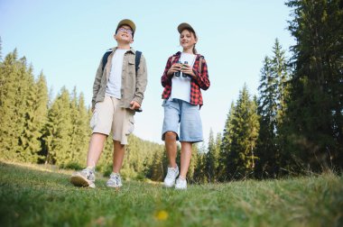 İki genç turist yemyeşil bir ormanda yürüyüş yapıyor, güzel manzaranın tadını çıkarıyor ve dürbünle doğayı keşfediyorlar.