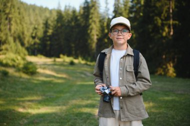 Elinde klasik kamerayla izci çocuk, ormanda yürüyüş yaparken doğayı keşfediyor, yaz tatilinin ve seyahat macerasının tadını çıkarıyor.